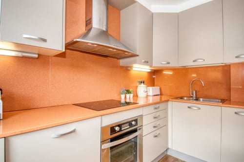 Modern kitchen with orange backsplash, white cabinets, stainless steel appliances at Finques Garcia Enrich apartment in