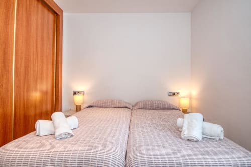 Modern bedroom with two twin beds, striped bedding, wooden door, bedside lamps, and white towels at Finques Garcia Enrich