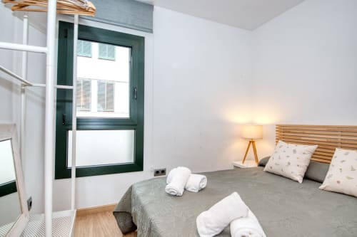 Modern bedroom in Palafrugell apartment with wooden headboard, white towels, bedside lamp, green door, and hardwood flooring