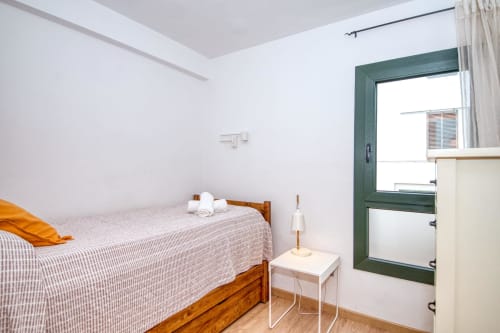 Bright bedroom in Palafrugell apartment near Canadell beach with wooden bed, white linens, green-framed window, and
