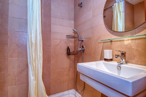Modern bathroom with orange tile walls, white sink, handheld showerhead, and round mirror in Palafrugell apartment