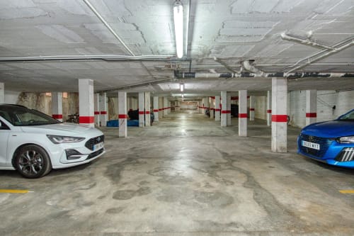 Underground parking garage at Finques Garcia Enrich apartment complex in Palafrugell with white and blue cars, concrete