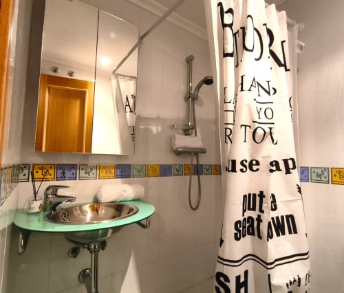 Baño moderno del apartamento Holibai en Baiona con lavamanos verde menta, espejo, ducha y texto decorativo en toalla