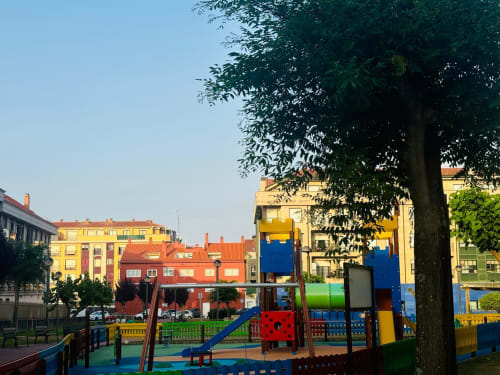 Colorido parque infantil con toboganes y equipos para escalar en la plaza de Baiona, rodeado de vibrantes edificios residenciales