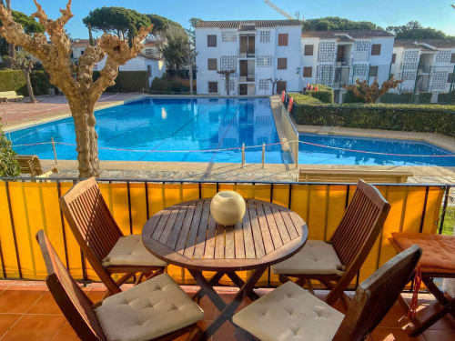 Patio avec table en bois, chaises et parasol dominant les piscines de l'hôtel Finques Garcia Enrich à Palafrugell