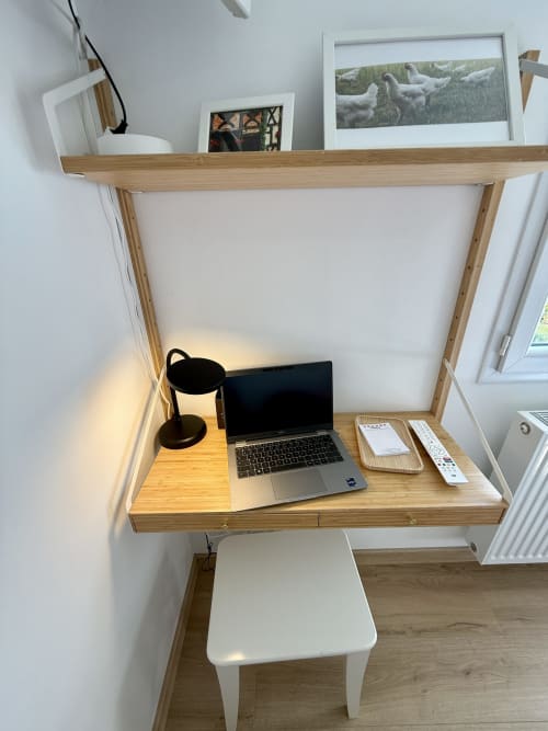 Wall-mounted desk area in the Bresse room with wooden shelf, black desk lamp, laptop, and remote control.