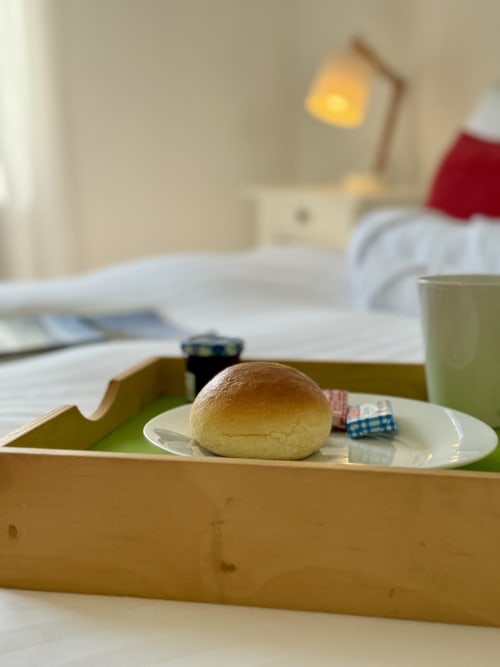 Double bed in the Bresse room with white sheets, red throw and cushions, and a green breakfast tray on the bed.