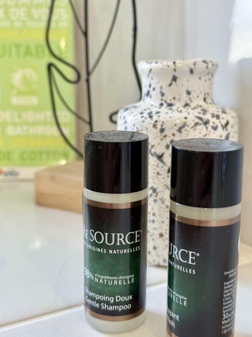 Primo piano sui prodotti cortesia della camera Bugey: mini flaconi di shampoo e bagnoschiuma “Pure Source” al 98 % di origine naturale.