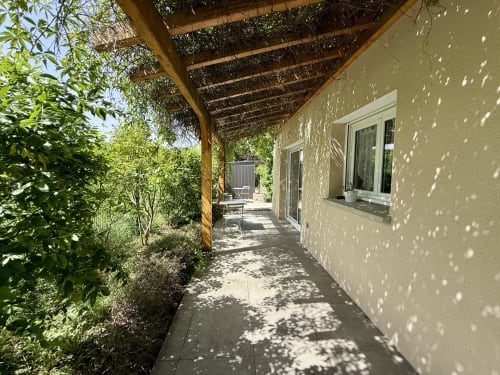Vialetto piastrellato lungo la facciata del gîte, protetto da una pergola coperta di vite, per un accesso ombreggiato alla terrazza.