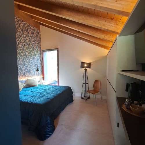Modern bedroom at Locanda del Sasso Rooms in Crodo with blue bedding, wooden ceiling, and mountain view through glass door.