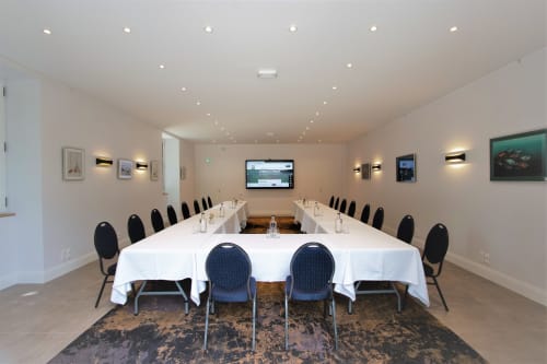 Modern conference room at Domaine de La Briandais with U-shaped table setup, blue chairs, and wall-mounted screen