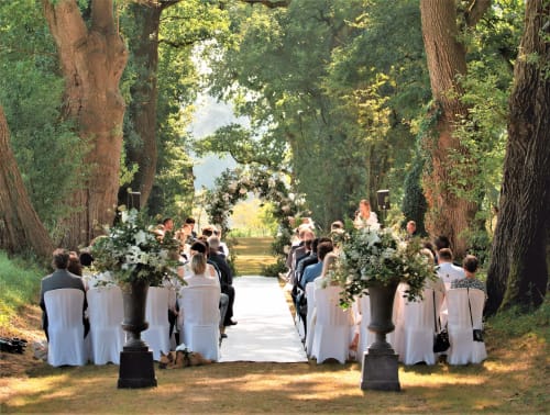 Outdoor wedding ceremony at Domaine de La Briandais in Missillac, France, with guests seated under tall trees and floral