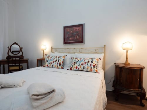 Elegante camera da letto al SleepWithMe Luxury B&B di Pisa con letto color crema, cuscini colorati, comodini antichi e illuminazione calda