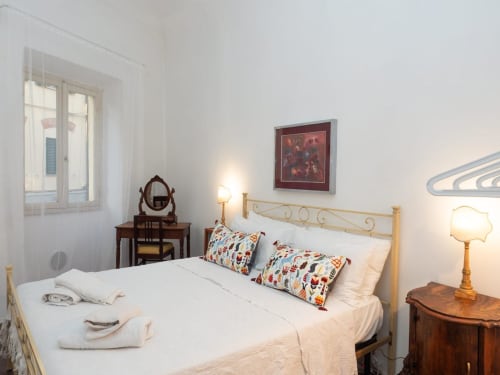 Camera luminosa nel SleepWithMe Luxury B&B di Pisa con letto in legno, cuscini colorati, mobili vintage e luce naturale
