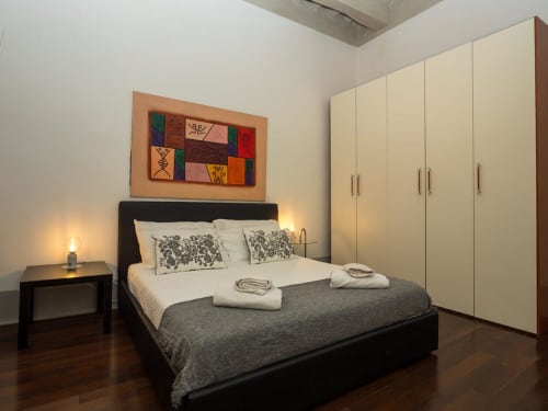 Camera moderna presso SleepWithMe Luxury B&B a Pisa con letto nero, armadio color crema e opere d'arte colorate