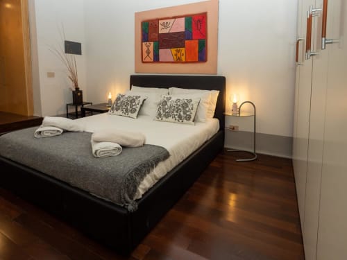 Moderna camera da letto al SleepWithMe Luxury B&B di Pisa con letto nero, biancheria bianca, opere d'arte colorate e pavimento in legno scuro.