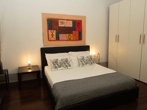 Camera da letto moderna presso SleepWithMe Luxury B&B Pisa con letto nero, cuscini bianchi, arte murale colorata e guardaroba color crema