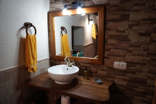 Modern bathroom with circular white sink, wooden vanity, lighted mirror, and yellow towels at Casonas de Marengo cottage in