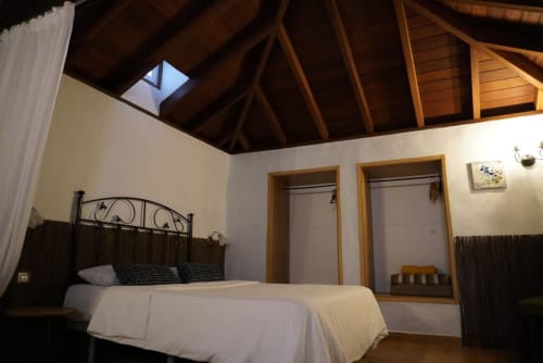 Modern cottage bedroom at Casonas de Marengo with wooden beam ceiling, metal bed frame, and dual closets overlooking Icod de