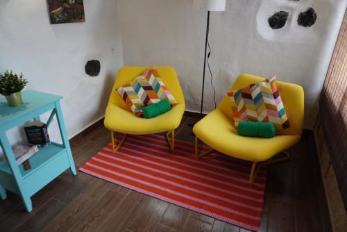 Colorful cottage sitting area with two yellow chairs, geometric pillows, turquoise side table, and striped rug at Casonas de