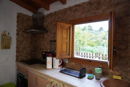 Rustic cottage kitchen at Casonas de Marengo with stone walls, modern appliances, and mountain views through large window in