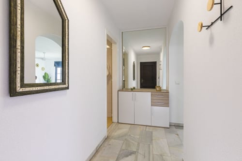Modern hallway in Marbella apartment with decorative mirror, white cabinetry, and marble flooring leading to bathroom