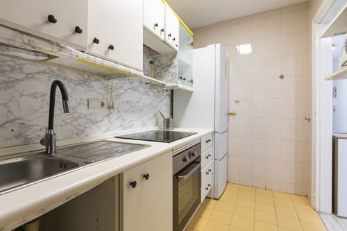 Modern kitchen in Marbella apartment with marble backsplash, white cabinetry, stainless steel appliances, and yellow tile