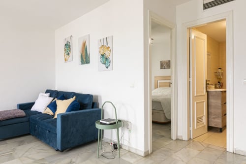 Modern apartment living area with blue sofa, plant artwork, and doorway to bedroom in Marbella Puerto Banús rental