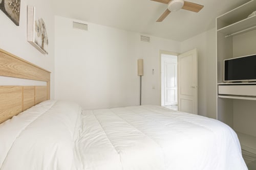 Bright, modern bedroom in Marbella apartment with wooden bed frame, white bedding, built-in wardrobe, and sea views