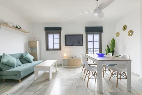 Modern open-plan apartment in Marbella with mint sofa, dining table, marble floors, TV, and sea views from windows