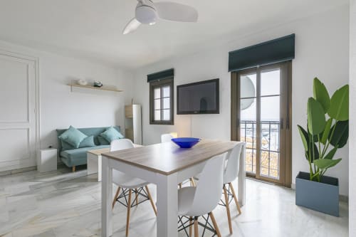 Modern open-plan living area in Marbella apartment with dining table, turquoise sofa, sea view, and ceiling fan