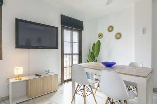 Modern apartment dining area in Marbella with sea view, featuring wooden table, white chairs, and contemporary decor