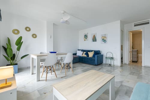 Modern open-plan living area in Marbella apartment with dining table, blue sofa, kitchen, and sea view decor