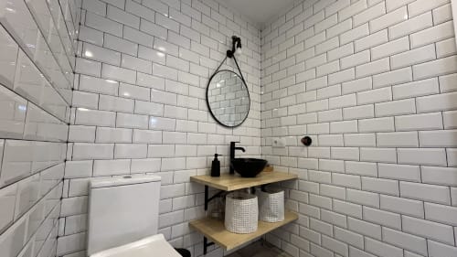 Baño moderno en apartamento Gestyp-AT de Mérida con azulejos subway, accesorios negros, vanidad de madera y espejo redondo.