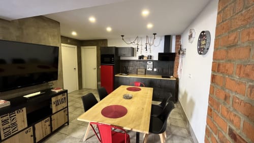 Cocina y comedor modernos en Mérida con mesa de madera, detalles rojos, pared de ladrillo visto y electrodomésticos negros