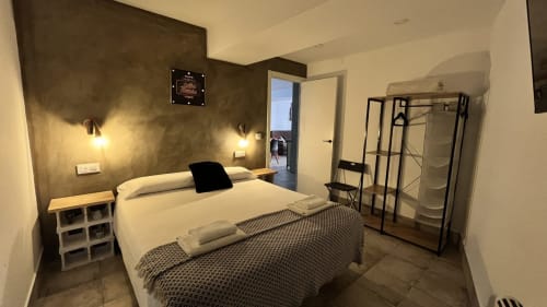 Elegante dormitorio moderno en Mérida con cama queen, pared de acento oscuro, iluminación de cabecera y acceso a vista de la ciudad por puerta abierta
