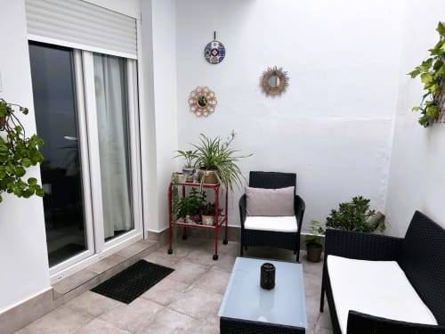 Balcón moderno en Mérida con asientos de mimbre negro, plantas en macetas, relojes decorativos y vistas a la ciudad.