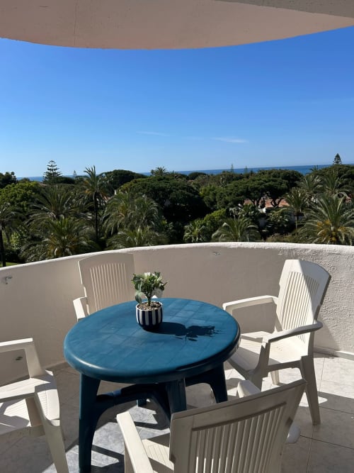 Terraza con mesa azul, sillas blancas y vistas al mar entre palmeras en Marbella