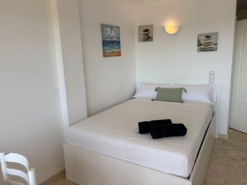 Dormitorio moderno en apartamento SACORO de Marbella con cama blanca, cuadros con vistas al mar y decoración costera