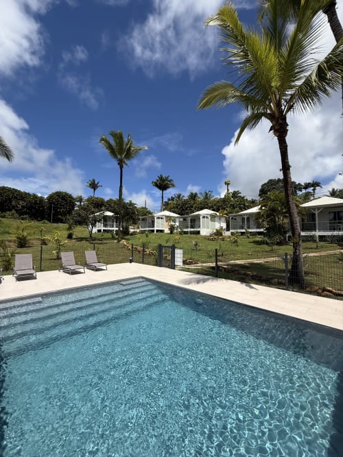 Piscine cristalline de la Domaine de la Glacière à Petit Bourg avec transats, palmiers et bungalows blancs