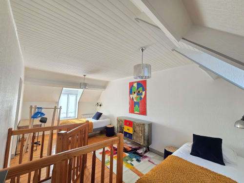 Modern loft bedroom at Relais des Iles cottage in Saint-Marcouf with wooden stairs, sea-view windows, and colorful artwork