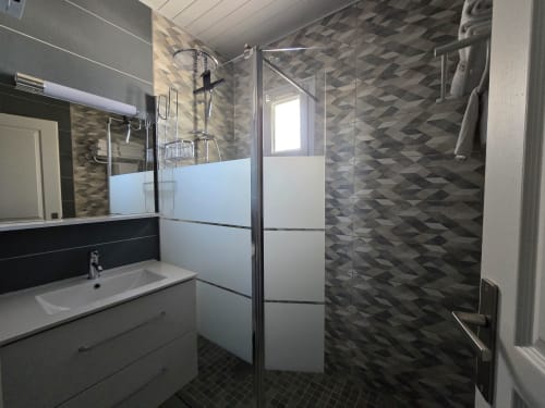 Modern bathroom with walk-in shower, geometric tile walls, vanity with mirror, and window at Relais des Iles cottage,