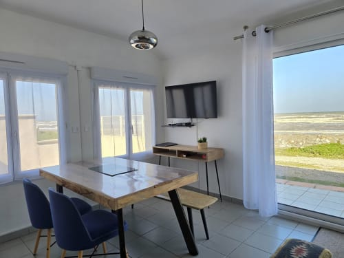 Modern cottage living room with sea view at Relais des Iles, featuring dining table, TV, and terrace access