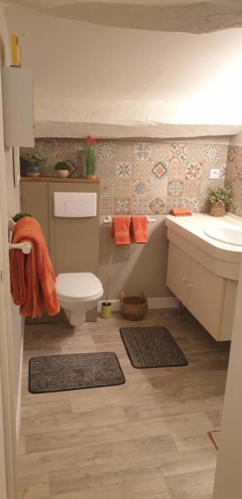Salle de bains moderne à La Maison de Philomène avec carrelage à motifs, lavabo, toilettes et accents orange à Corme-Royal