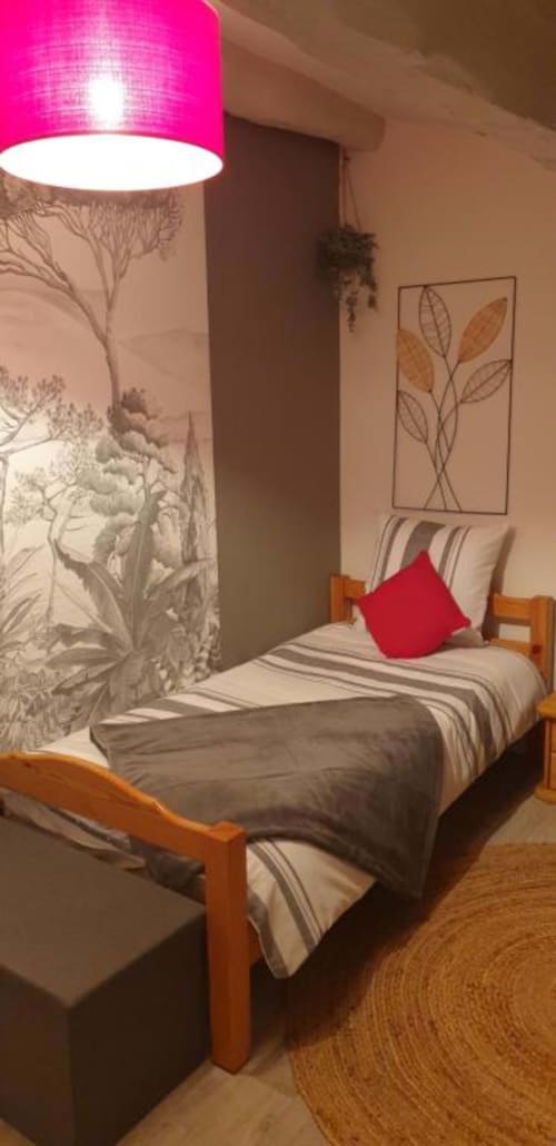 Chambre douillette à La Maison de Philomène avec lit en bois, coussin rouge, lampadaire rose vif et