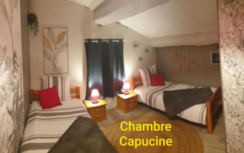 Chambre Capucine à La Maison de Philomène : lits jumeaux à literie rayée, oreillers rouges, tables de nuit en bois et vue sur le jardin
