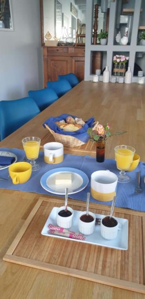 Élégante table à La Maison de Philomène : chaises bleues, verres de jus jaunes, panier à pain et dégustation de café