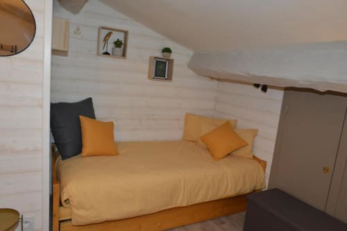 Chambre douillette à La Maison de Philomène avec lit jaune, oreillers orangés et murs chaulés