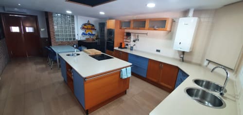 Cocina moderna de Villa Castelló Salou con armarios naranjas, encimeras blancas, isla central y fregaderos de acero inoxidable