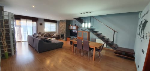 Moderna zona de estar diáfana en Villa Castelló Salou con suelos de madera, sofá negro, mesa de comedor, escaleras y chimenea de piedra